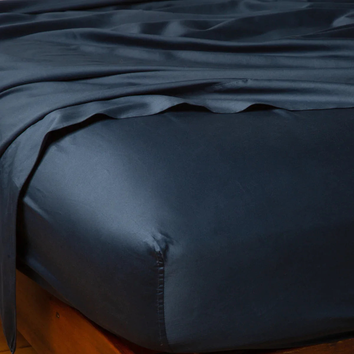 Midnight: Cotton sateen flat sheet draped over matching fitted sheet. Shown from the top corner, the flat sheet is rumpled, highlighting the shine of the fabric.
