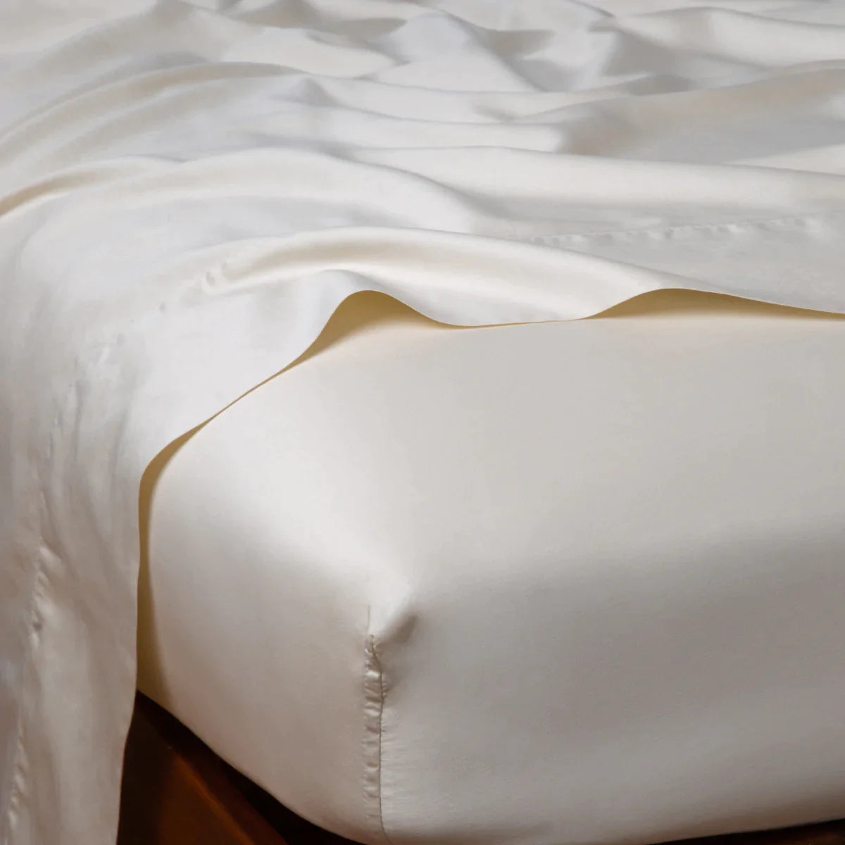 Parchment: Cotton sateen flat sheet draped over matching fitted sheet. Shown from the top corner, the flat sheet is rumpled, highlighting the shine of the fabric.