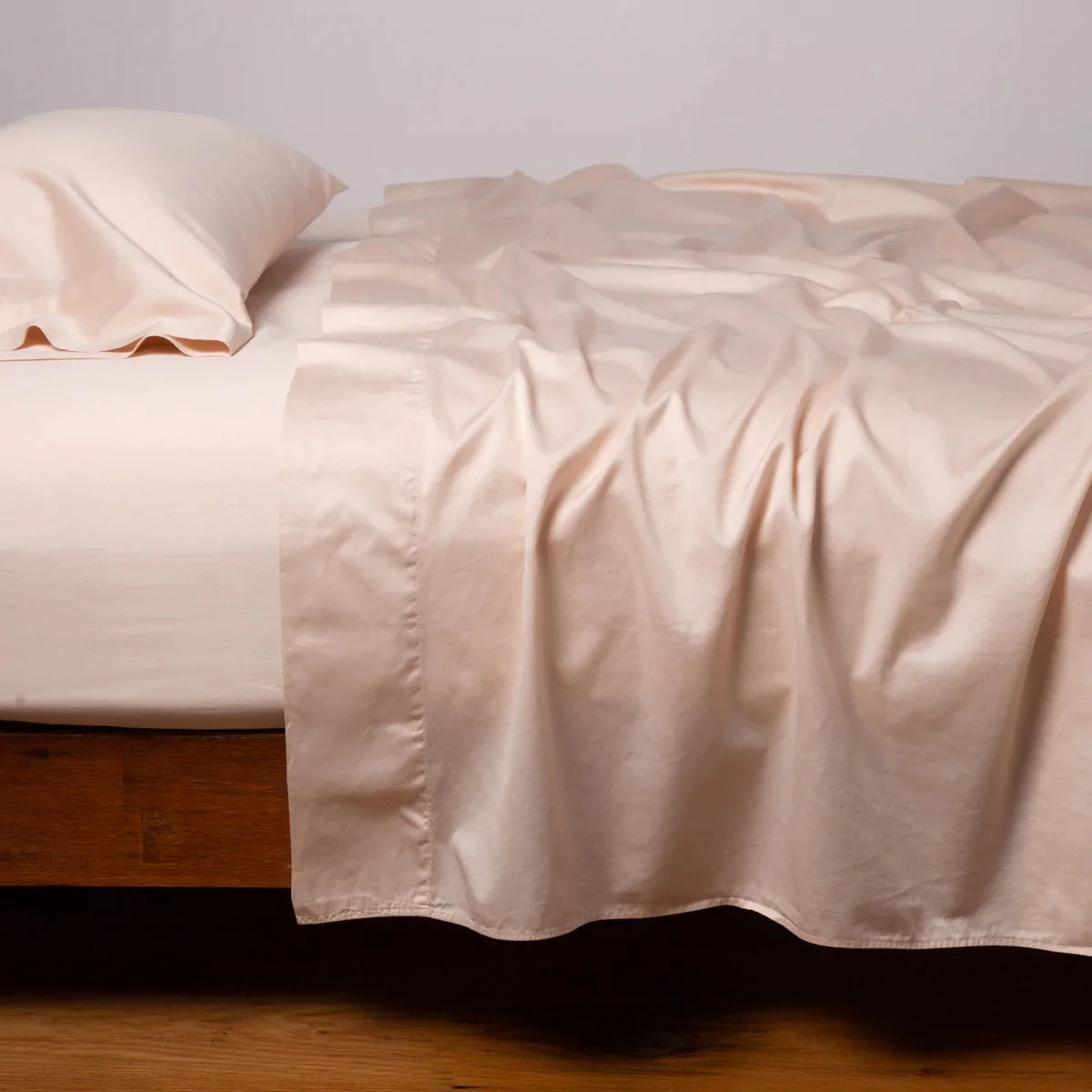 Pearl: Cotton sateen sleeping pillow, on a bed with matching sheets - side view.
