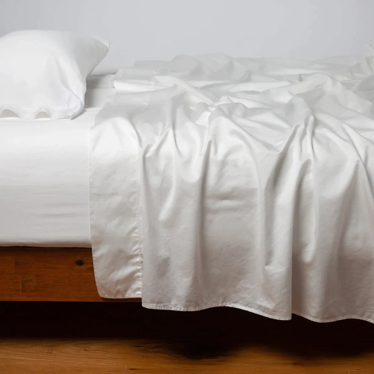 Winter White: Cotton sateen sleeping pillow, on a bed with matching sheets - side view.