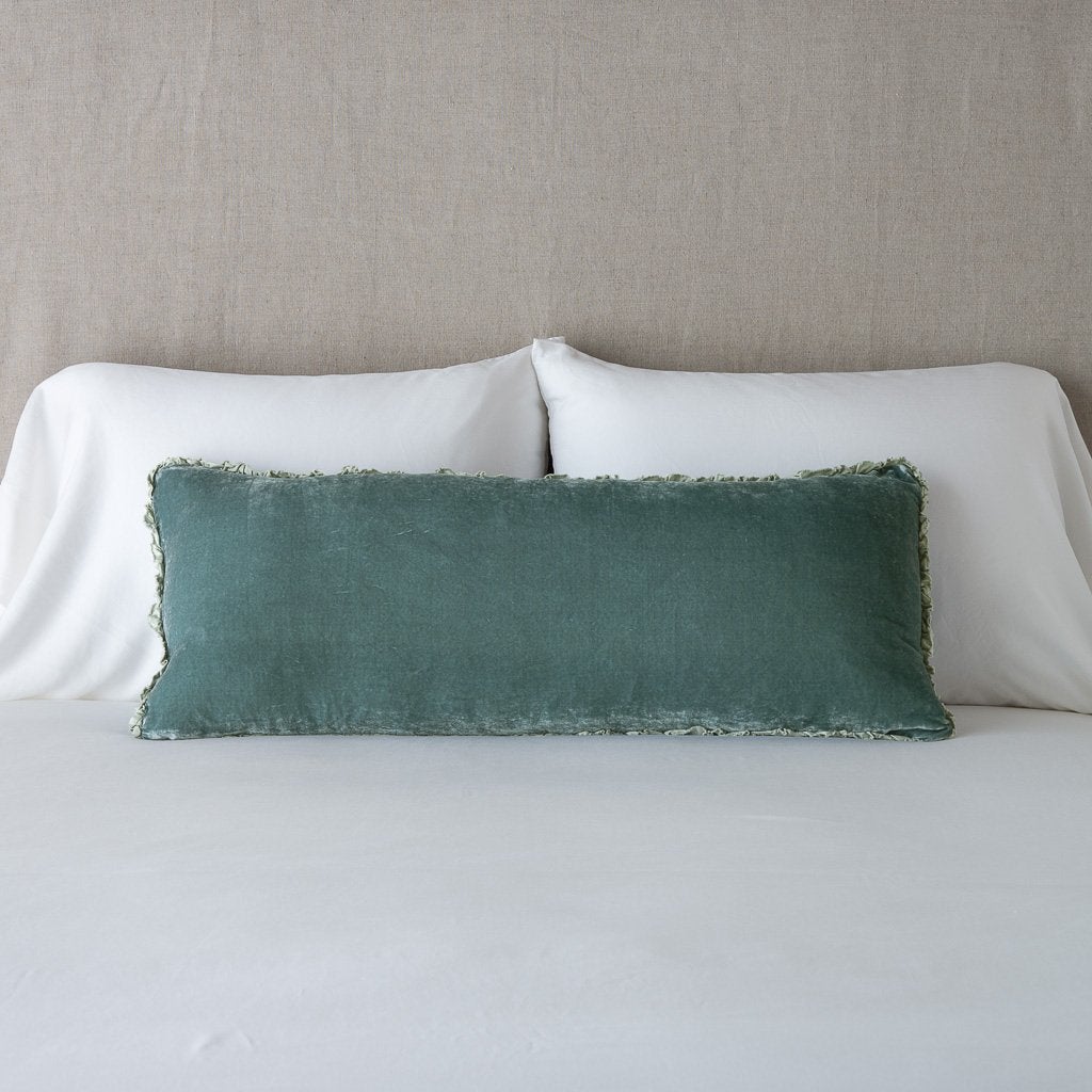 Eucalyptus: Silk velvet lumbar pillow with petite ruffle, leaning upright against neutral bedding and headboard.