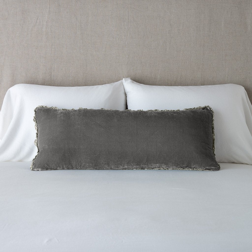 Fog: Silk velvet lumbar pillow with petite ruffle, leaning upright against neutral bedding and headboard.