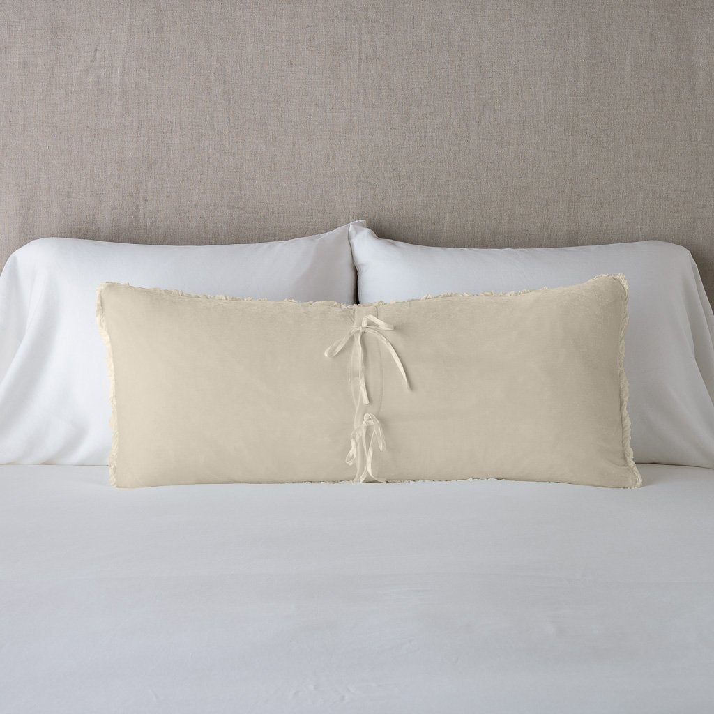 Parchment: Silk velvet lumbar pillow with petite ruffle leaning upright and backwards against neutral bedding and headboard, showcaseing the silk charmeuse tie closures.