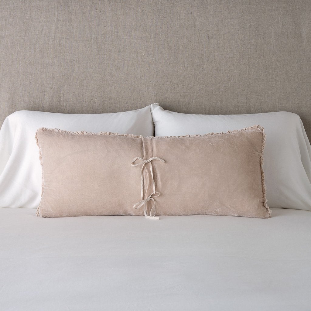 Pearl: Silk velvet lumbar pillow with petite ruffle leaning upright and backwards against neutral bedding and headboard, showcaseing the silk charmeuse tie closures.