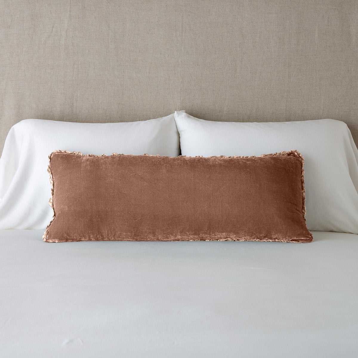 Rouge: Silk velvet lumbar pillow with petite ruffle, leaning upright against neutral bedding and headboard.