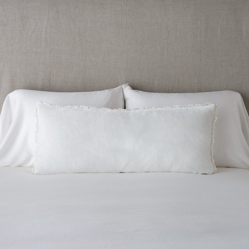 Winter White: Silk velvet lumbar pillow with petite ruffle, leaning upright against neutral bedding and headboard.