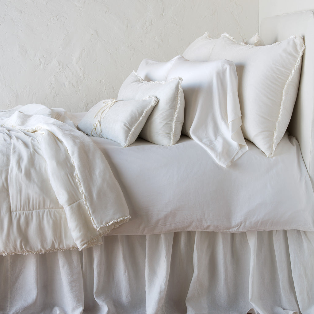 Winter White: Silk velvet throw blanket with petite ruffle, draped across a monochromatic bed - side view.