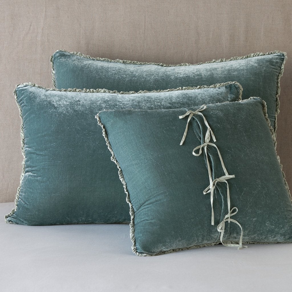 [allvariants]: Three carmen shams in eucalyptus leaning upright against a neutral headboard. The front sham is backwards, showcasing the charmeuse tie closures.