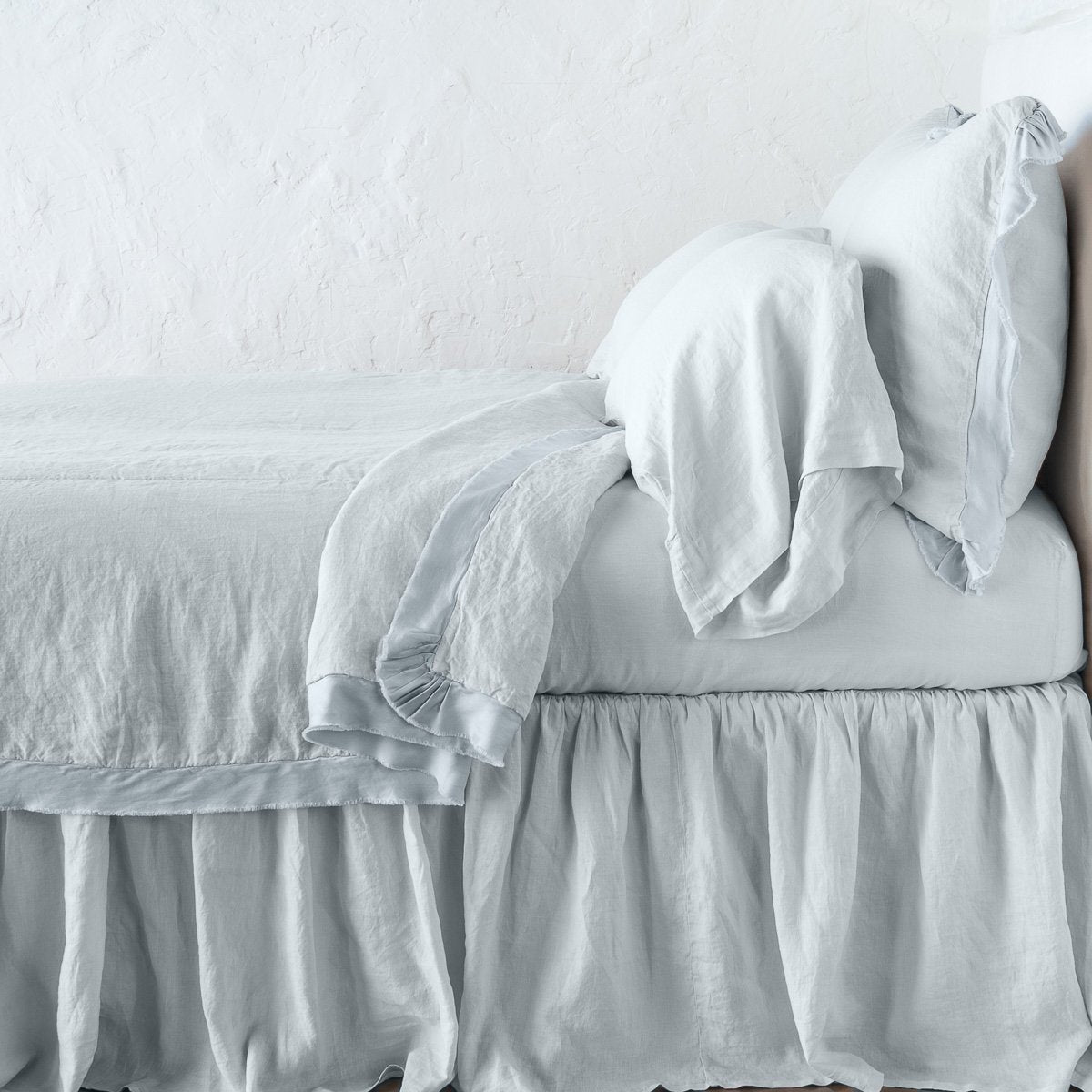 Cloud: satin trimmed linen coverlet on monochromatic bed with corner pulled back to reveal sheet, bed skirt - side view. 