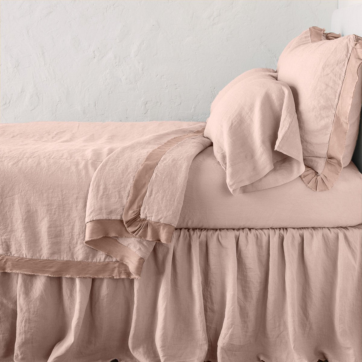 Rouge: satin trimmed linen coverlet on monochromatic bed with corner pulled back to reveal sheet, bed skirt - side view. 