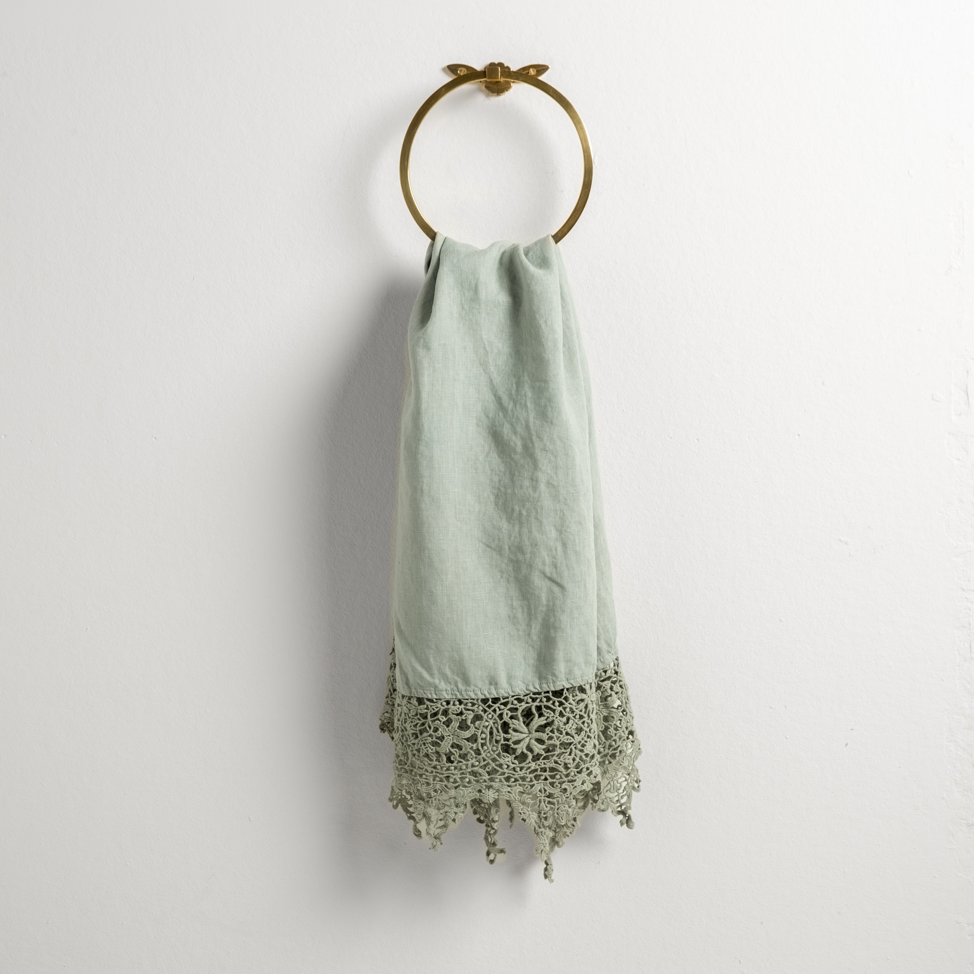 Eucalyptus: Lace trimmed linen guest towel  draped through a decorative towel ring against a plain white background.
