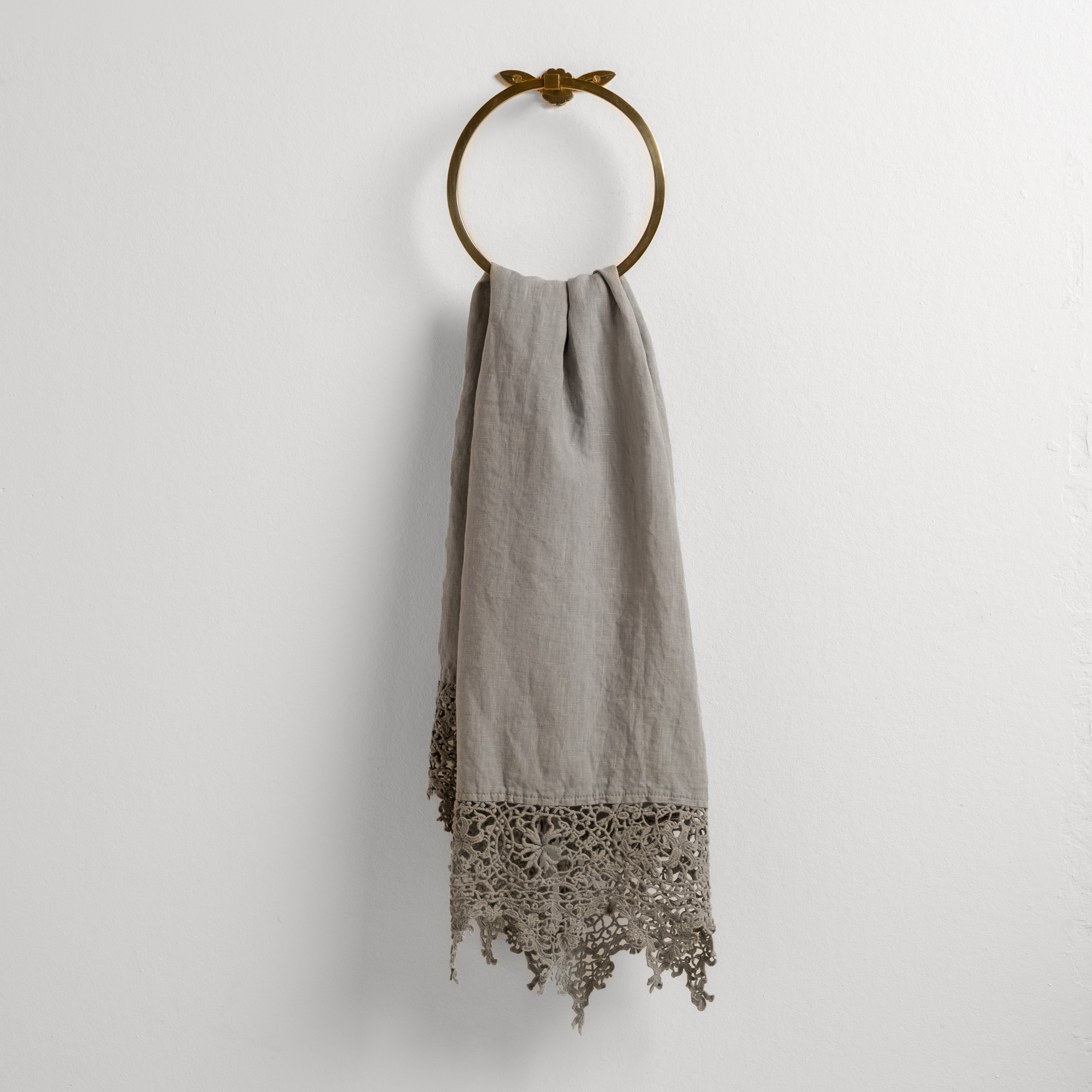 Mineral: Lace trimmed linen guest towel  draped through a decorative towel ring against a plain white background.