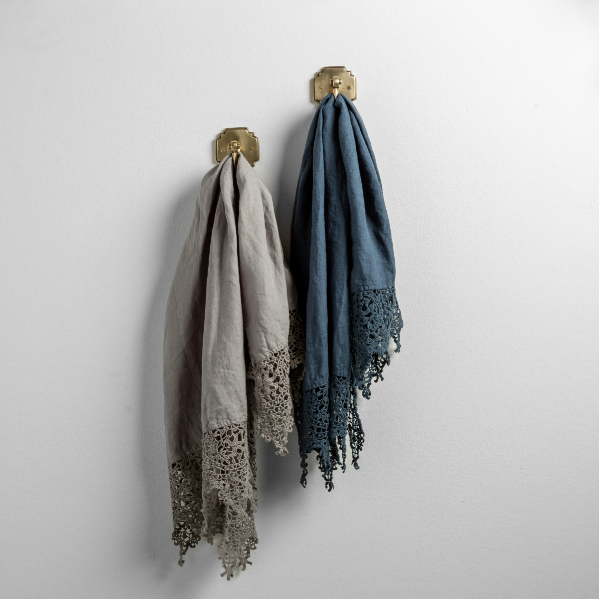: Two Frida guest towels, draped over decorative hooks against a white wall - moonlight and midnight.