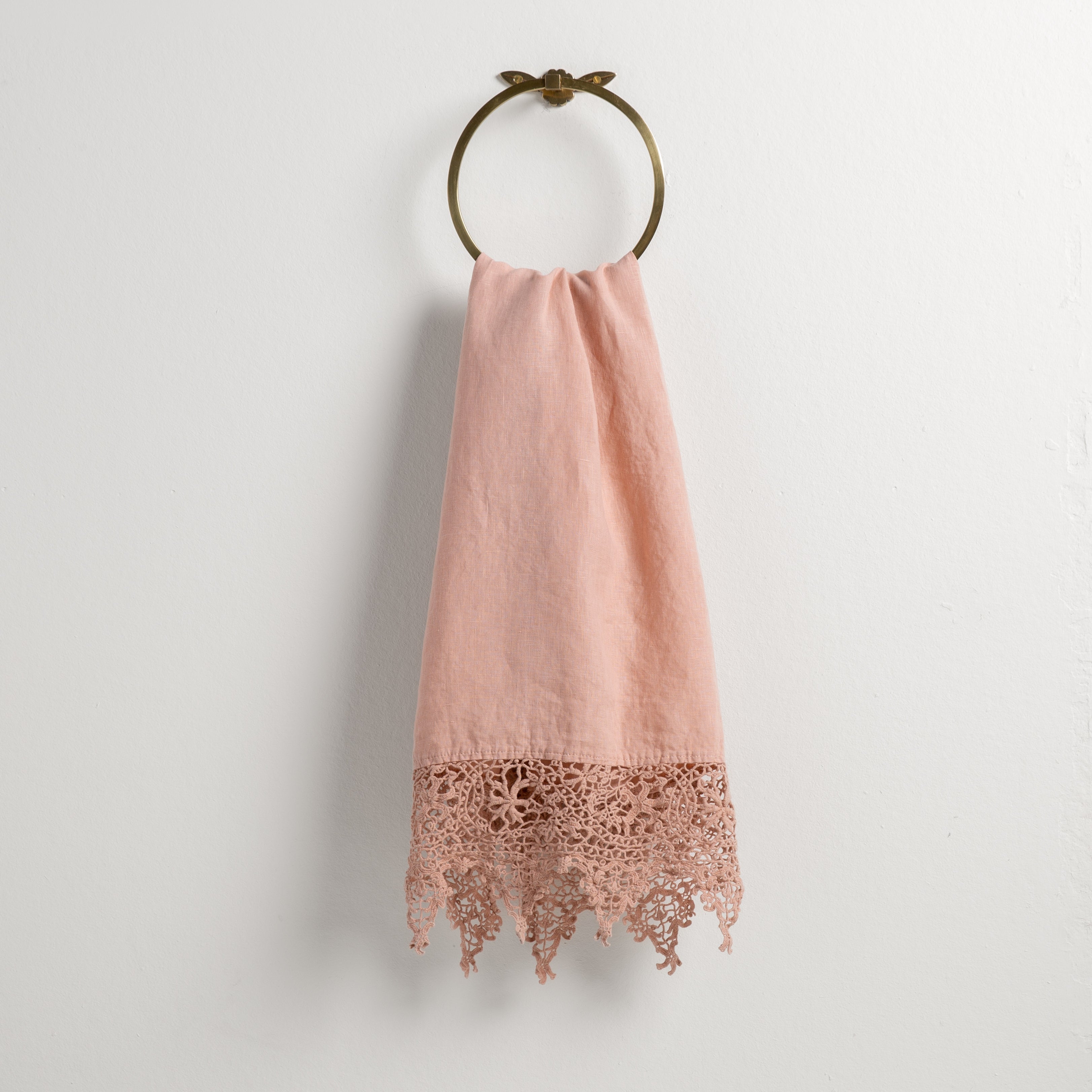 Rouge: Lace trimmed linen guest towel  draped through a decorative towel ring against a plain white background.
