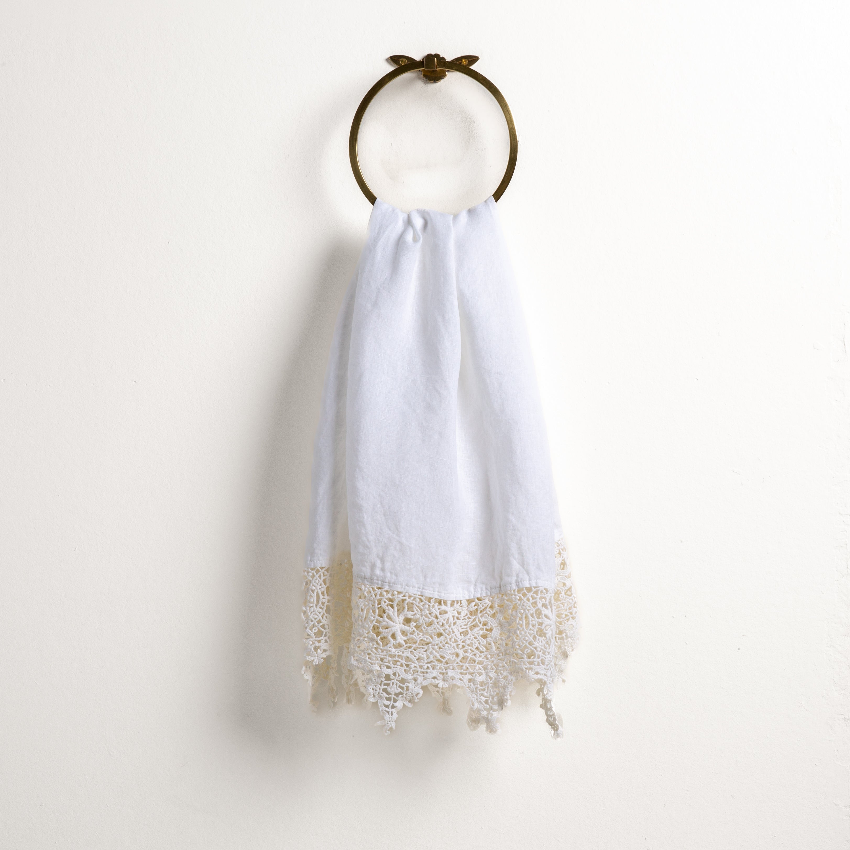 White: Lace trimmed linen guest towel  draped through a decorative towel ring against a plain white background.
