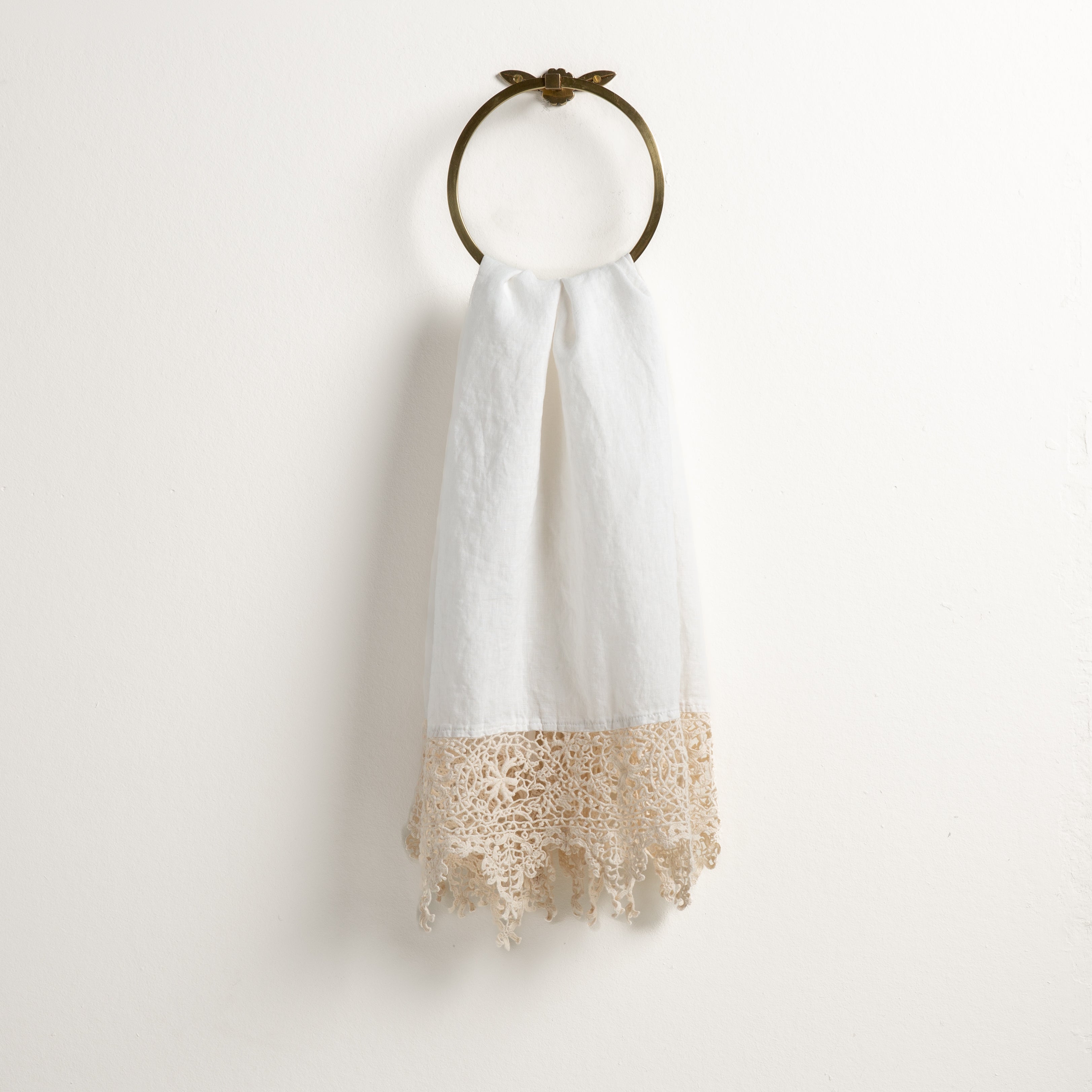 Winter White: Lace trimmed linen guest towel  draped through a decorative towel ring against a plain white background.