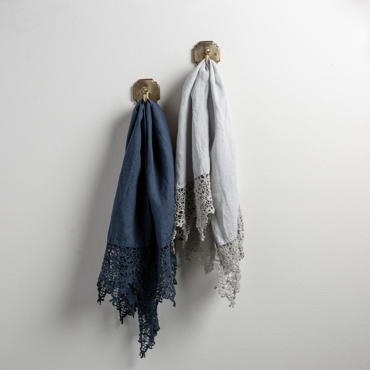 : Two Frida guest towels, draped over decorative hooks against a white wall - midnight and cloud.