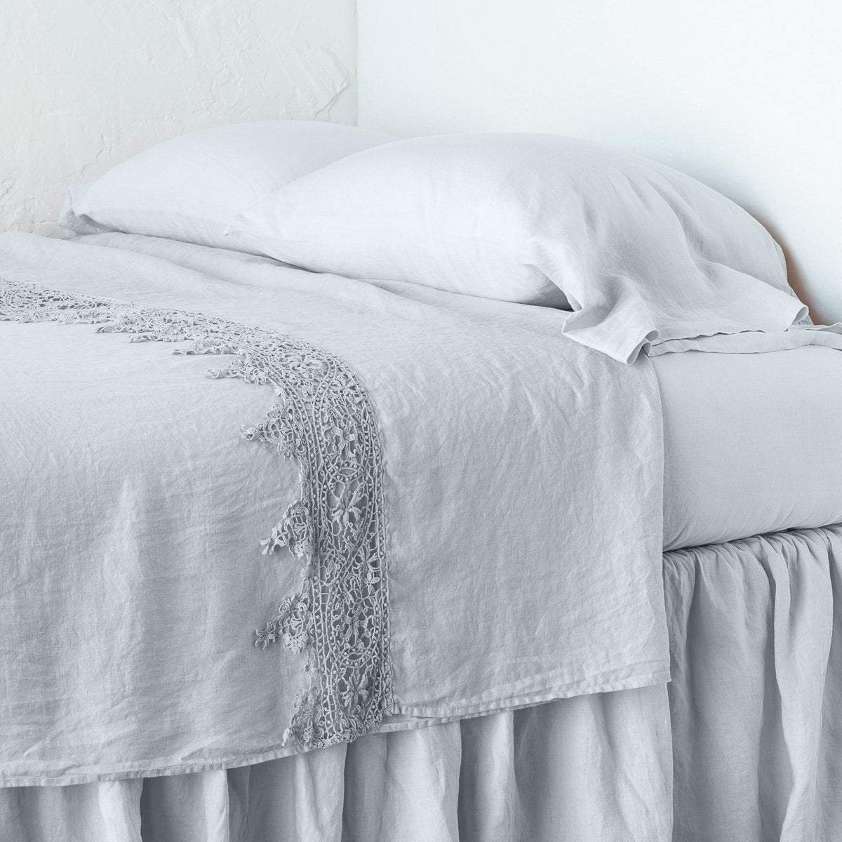 Cloud: Lace trimmed linen flat sheet neattly folded back on a monochromatic linen bed - cropped three-quarter angle.