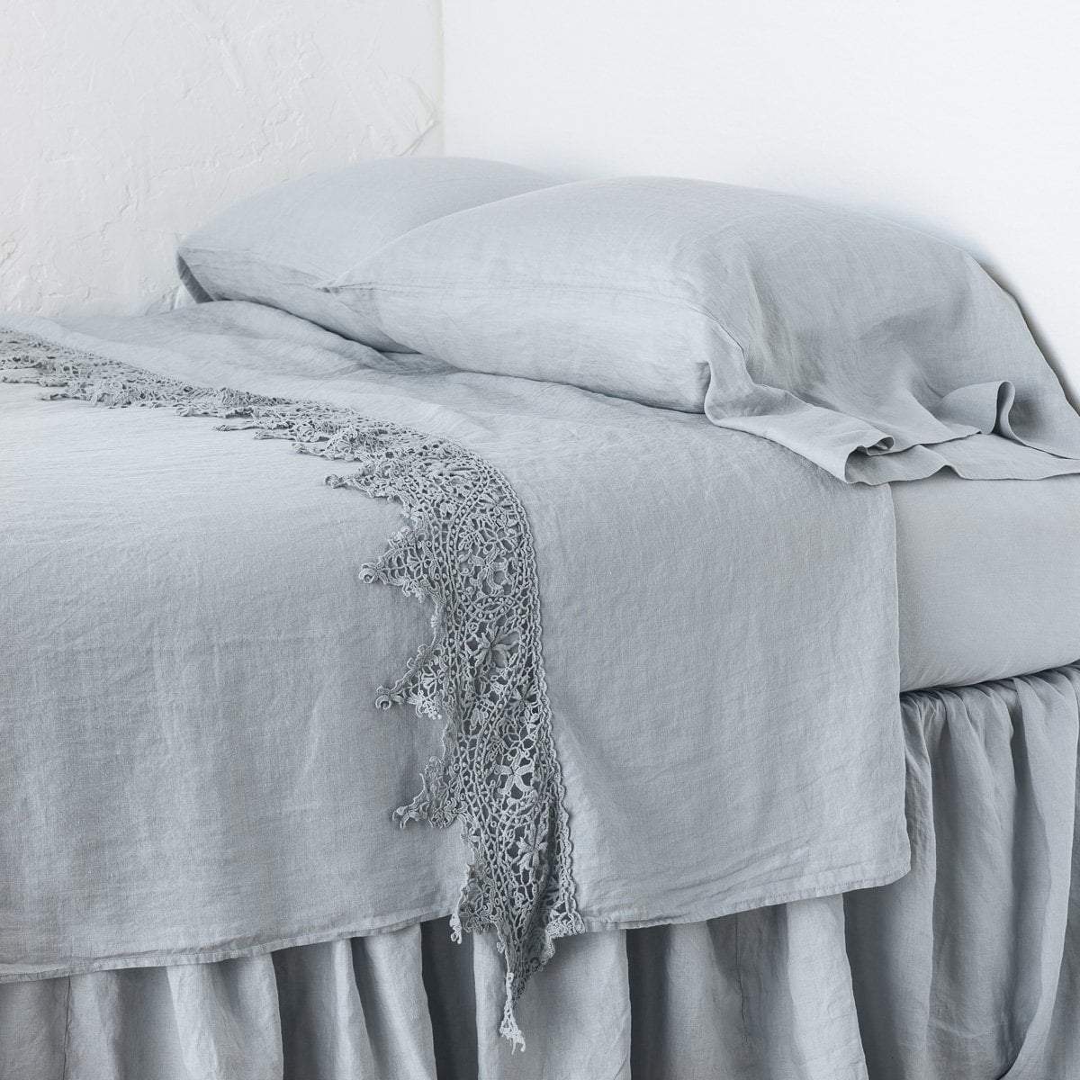 : Frida flat sheet in cloud, neatly folded back on a monochromatic linen bed - cropped three-quarter angle.