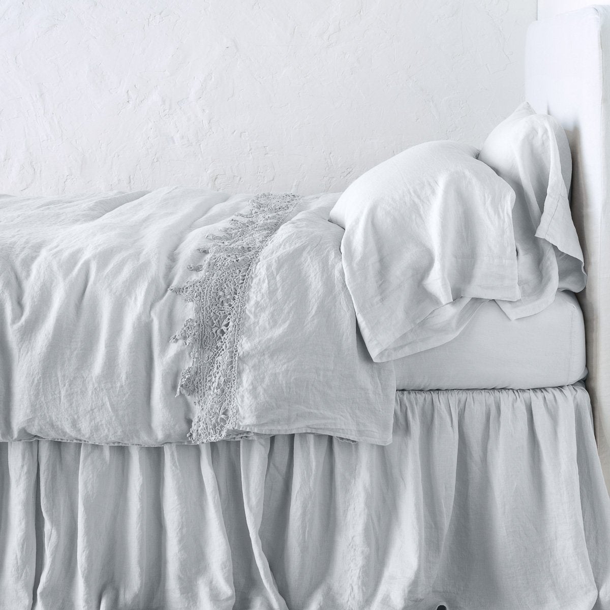 Sterling: Lace trimmed linen flat sheet folded back over monochromatic linen bed - side view. 
