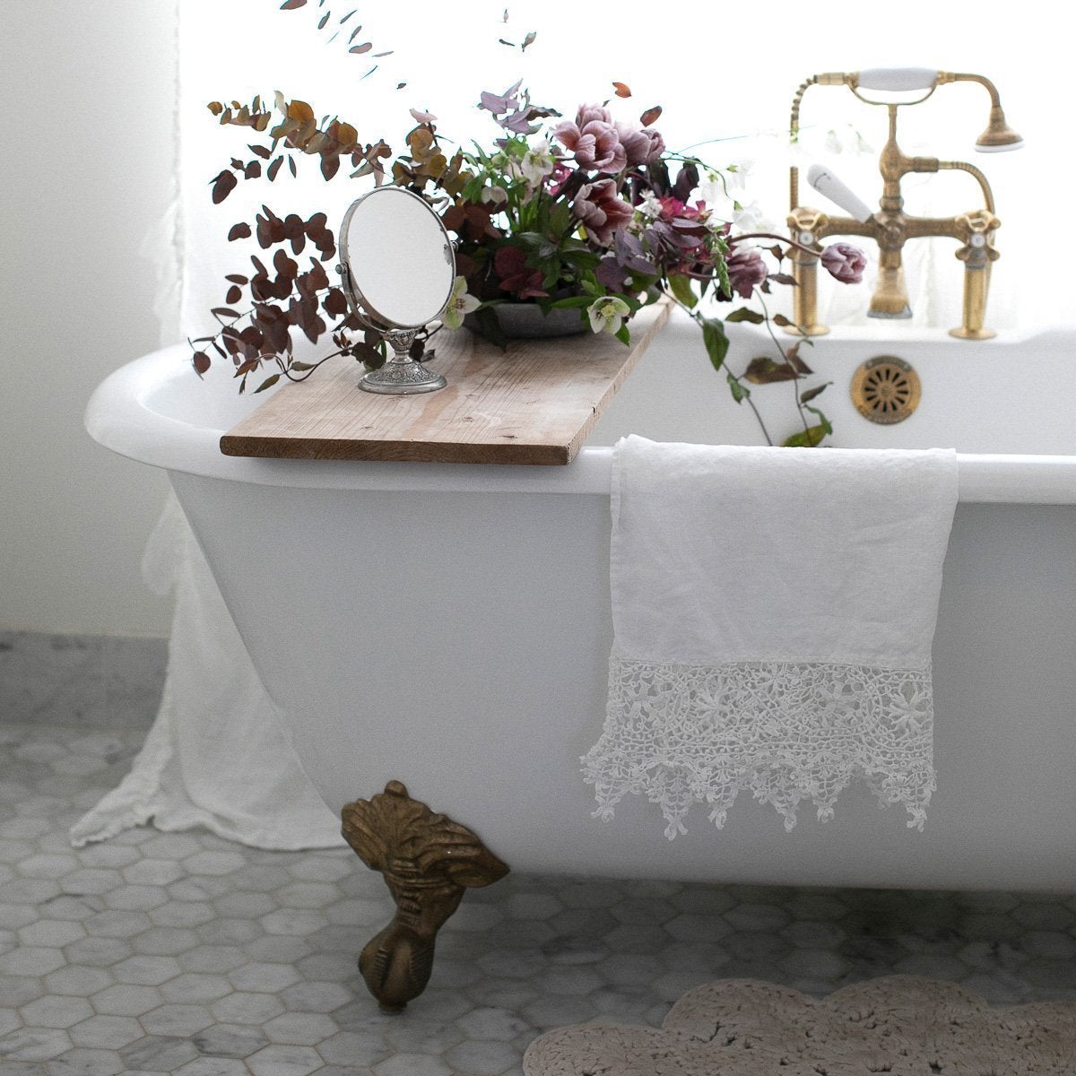 [allvariants]: White Frida guest towel draped over the edge of an antique tub, with copper accents and lavender and green floral bouquet.