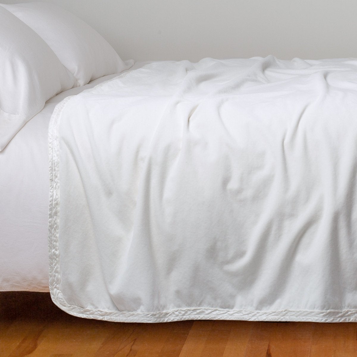 White: Cotton velvet bed end sized  blanket, draped on a white bed - side view.