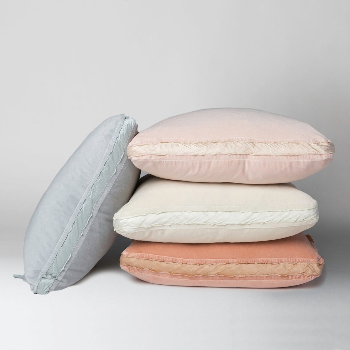 : Harlow 24 by 24 pillows stacked neatly against a plain background, in soft pink, cream and blue - side view.