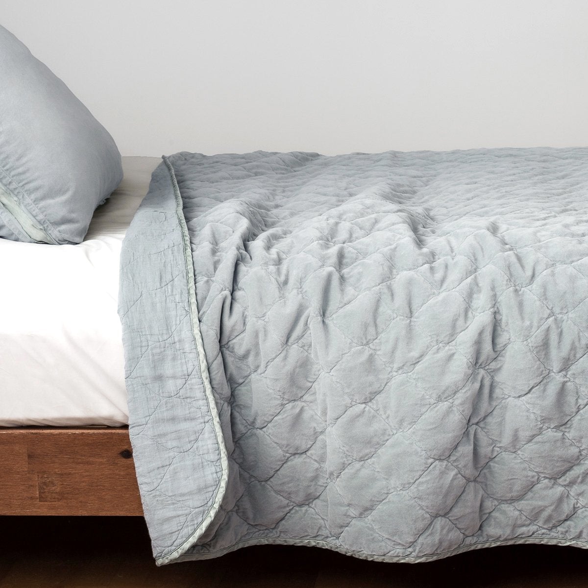 Cloud: Quilted cotton velvet coverlet, with top folded back to showcase linen back, draped over a white fitted sheet - side view.