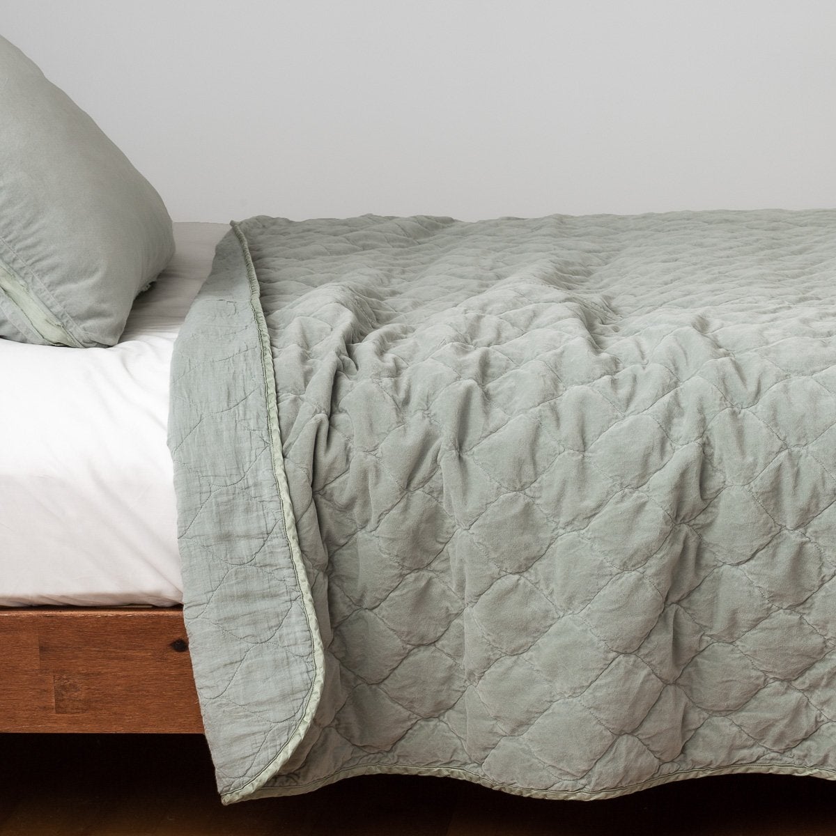 Eucalyptus: Quilted cotton velvet coverlet, with top folded back to showcase linen back, draped over a white fitted sheet - side view.