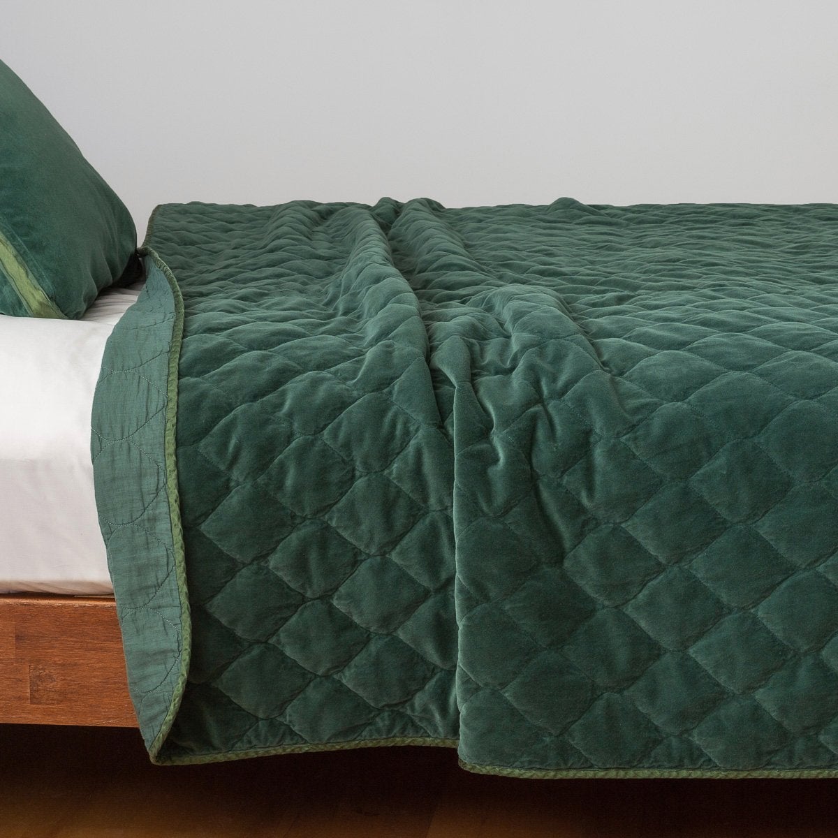 Jade: Quilted cotton velvet coverlet, with top folded back to showcase linen back, draped over a white fitted sheet - side view.