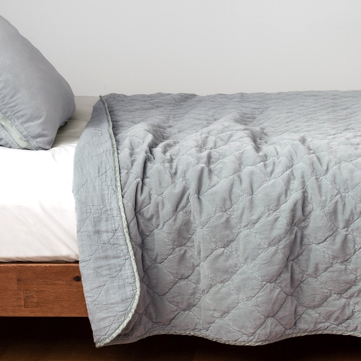 Mineral: Quilted cotton velvet coverlet, with top folded back to showcase linen back, draped over a white fitted sheet - side view.