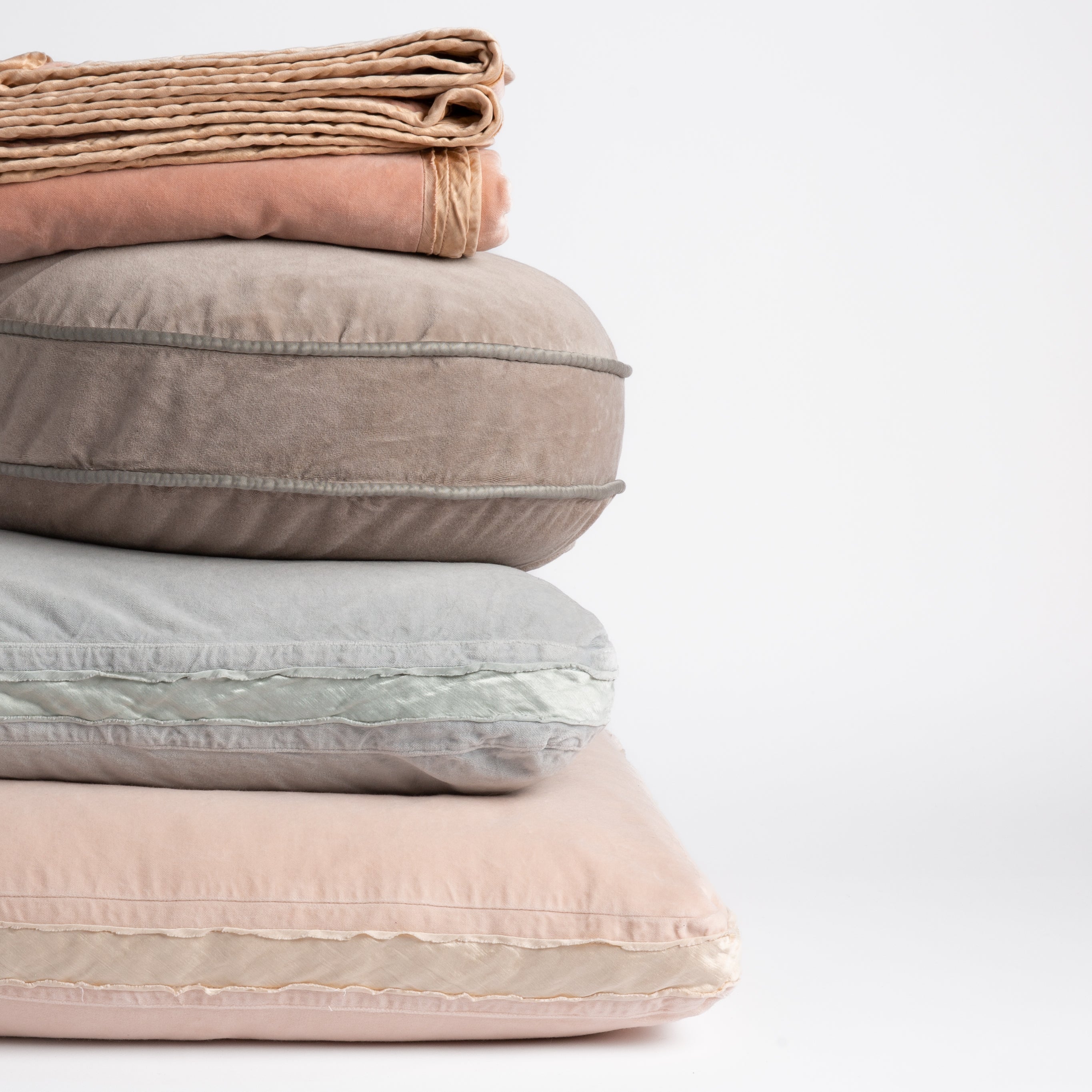 : stack of cotton velvet living pieces: throw blanket in rouge, 18" round pillow in fog, 18" square in cloud and 24" square pillow in pearl straight on against a white background.  The different trim details visible on each piece. 