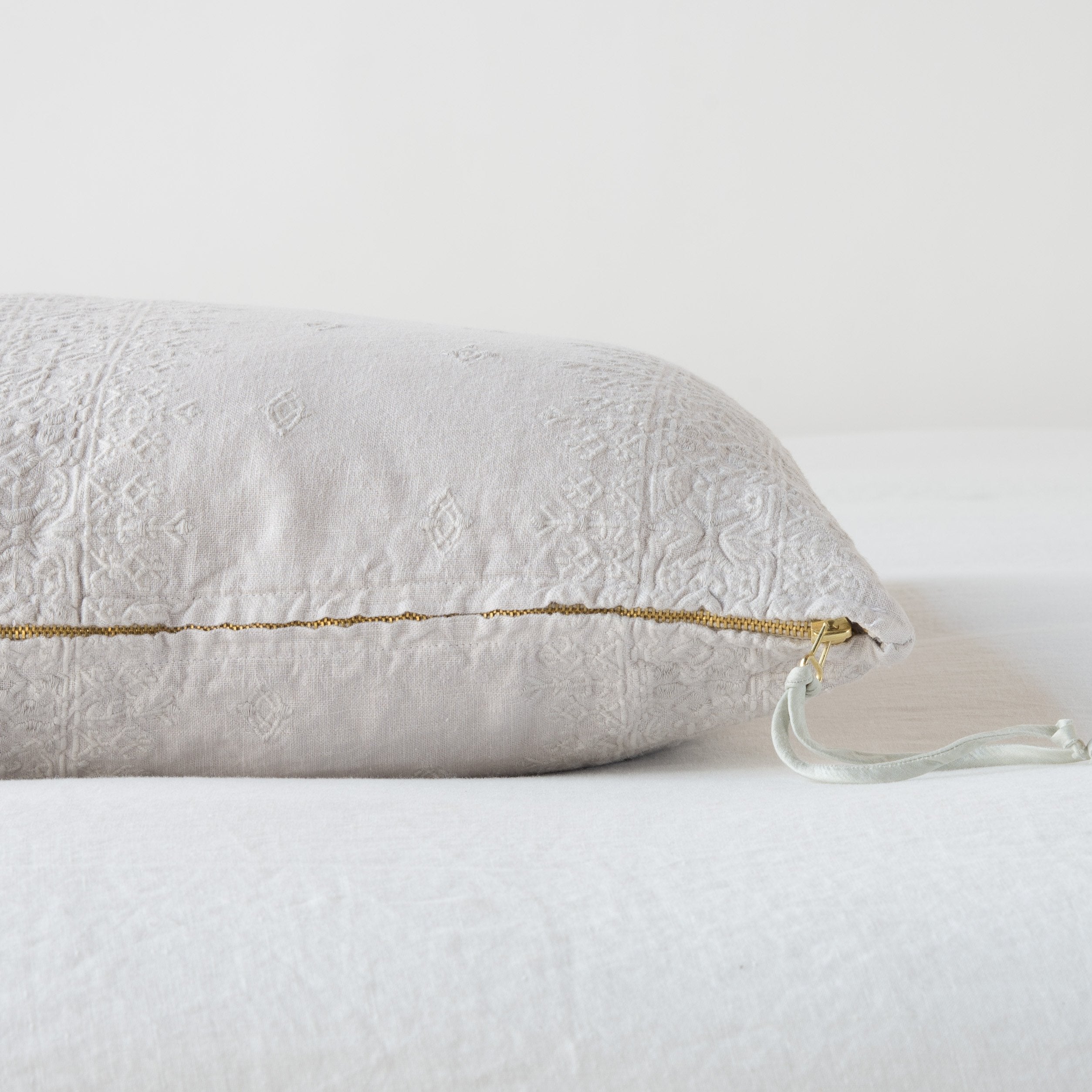 Sterling: Close-up of brass zipper and charmeuse pull details on throw pillow - side view.