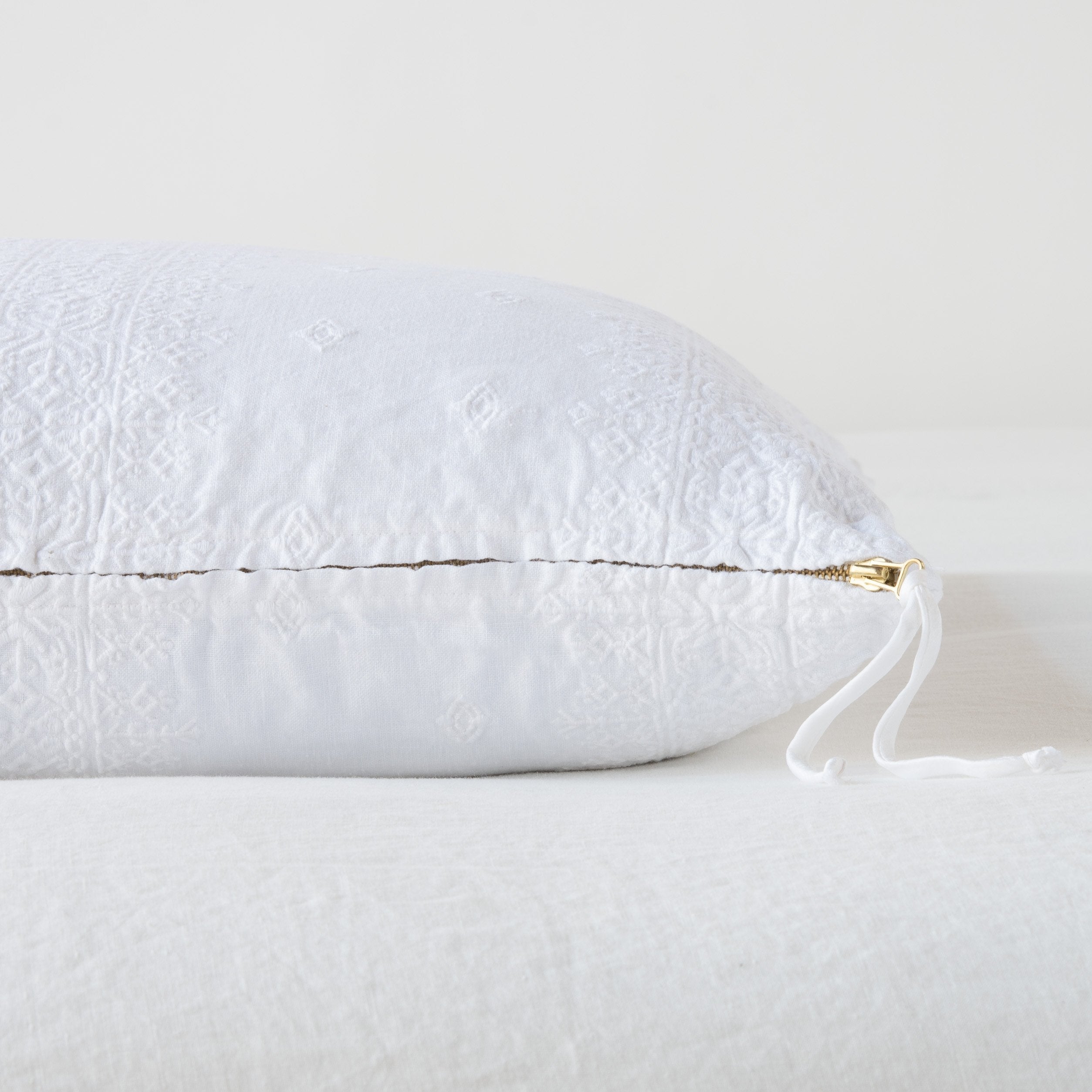 White: Close-up of brass zipper and charmeuse pull details on throw pillow - side view.