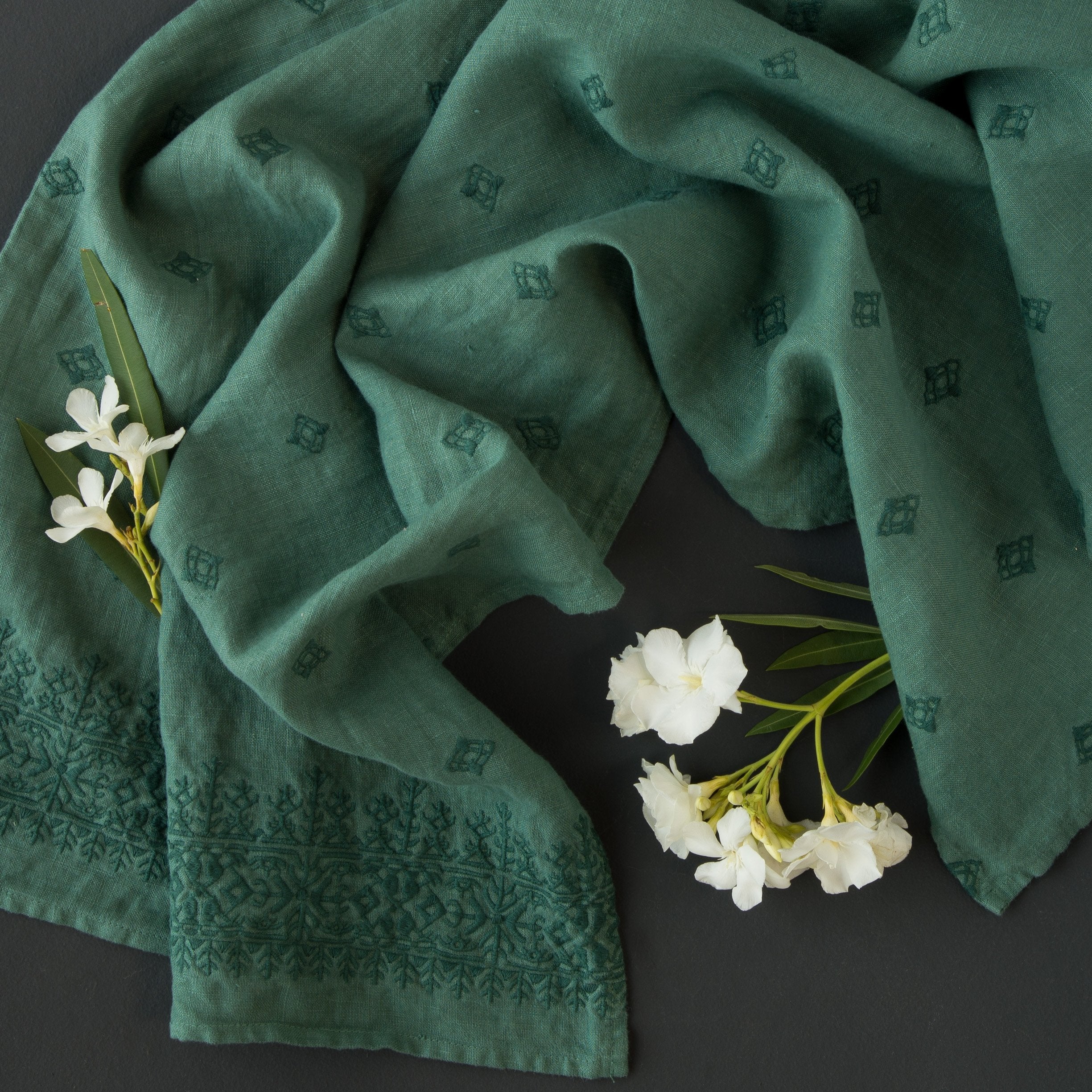 Jade: guest towel draped on a dark background scattered with delicate white flowers - overhead view.