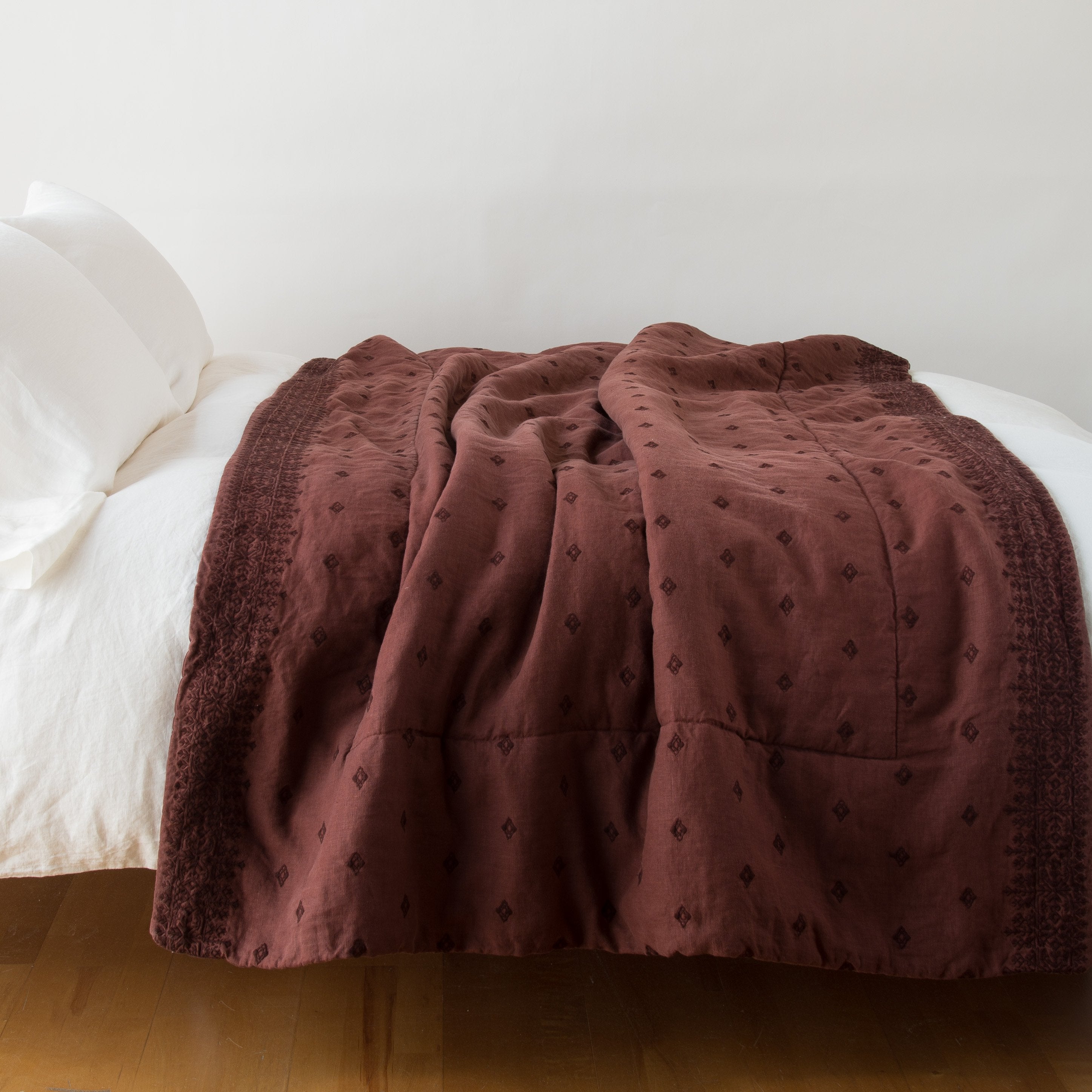 : Ines throw blanket in mahogany, draped over a simple white bed - side view.