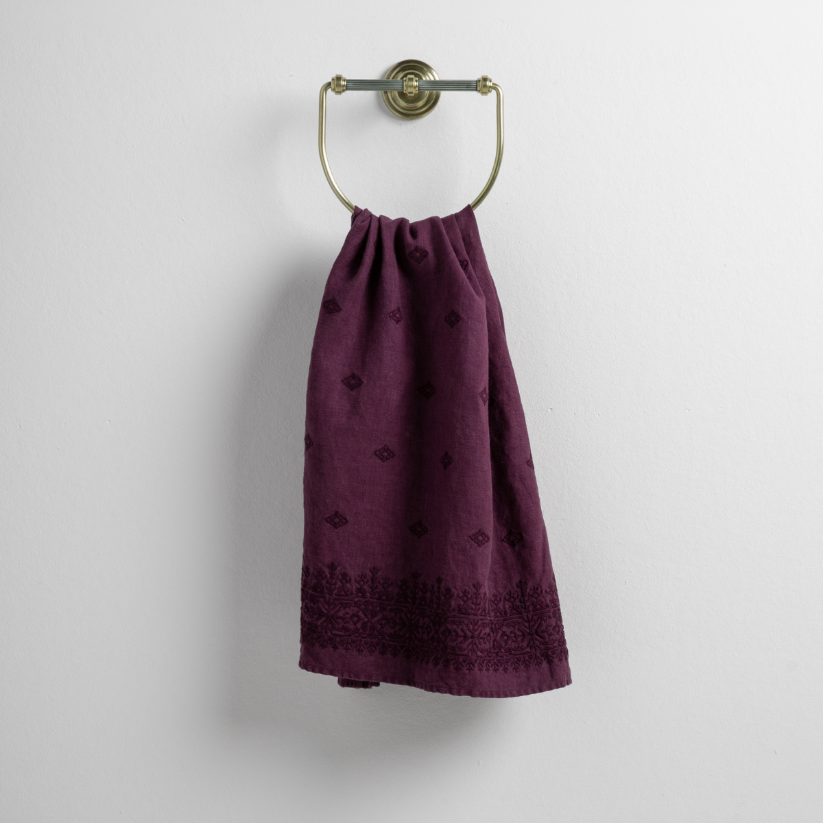 Fig: guest towel draped through a decorative brass towel ring against a white background.