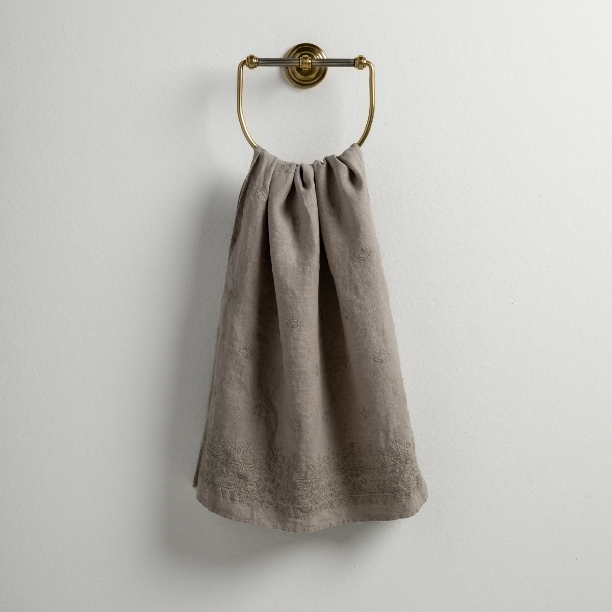 Fog: guest towel draped through a decorative brass towel ring against a white background.