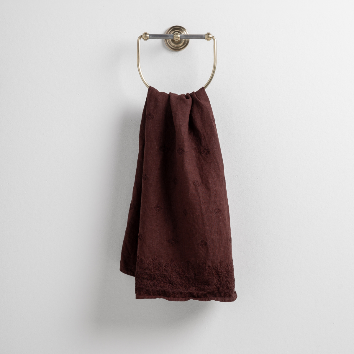 Mahogany: guest towel draped through a decorative brass towel ring against a white background.