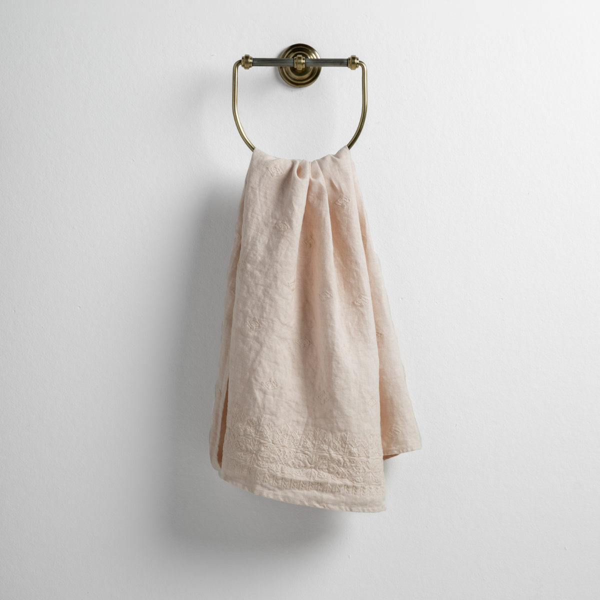 Pearl: guest towel draped through a decorative brass towel ring against a white background.