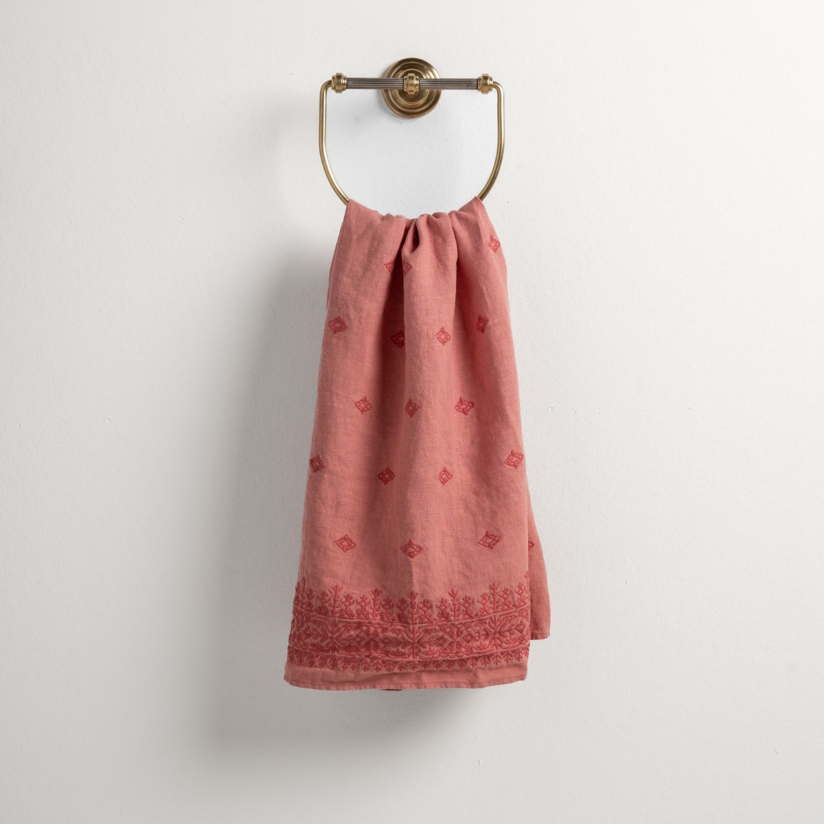 Poppy: guest towel draped through a decorative brass towel ring against a white background.