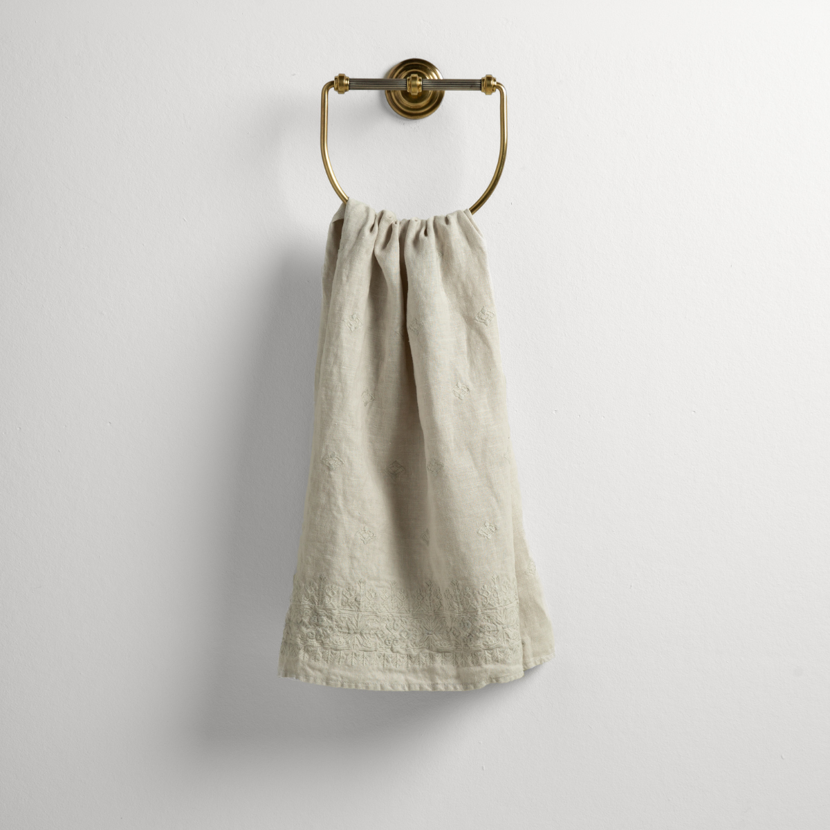 Sterling: guest towel draped through a decorative brass towel ring against a white background.