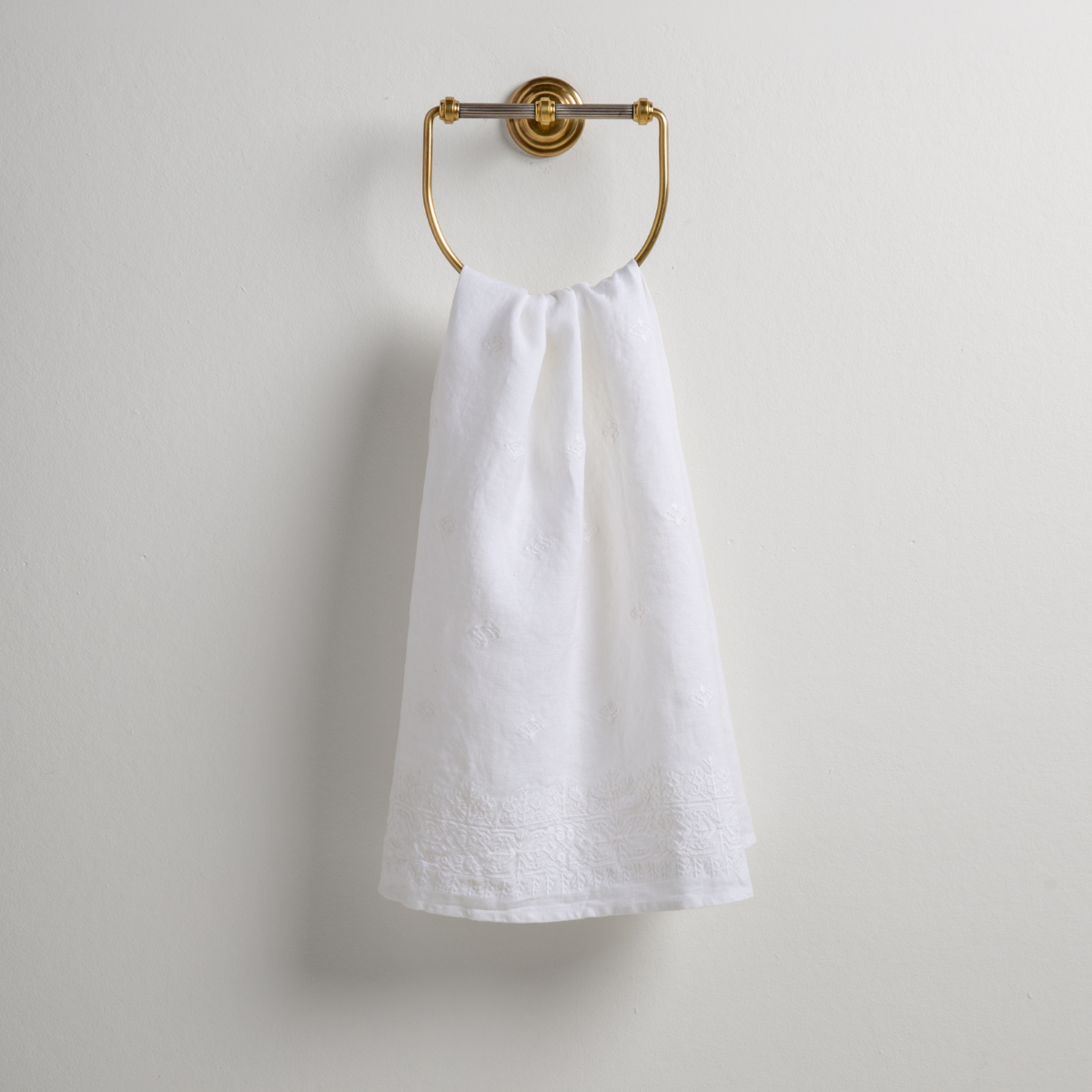 White: guest towel draped through a decorative brass towel ring against a white background.