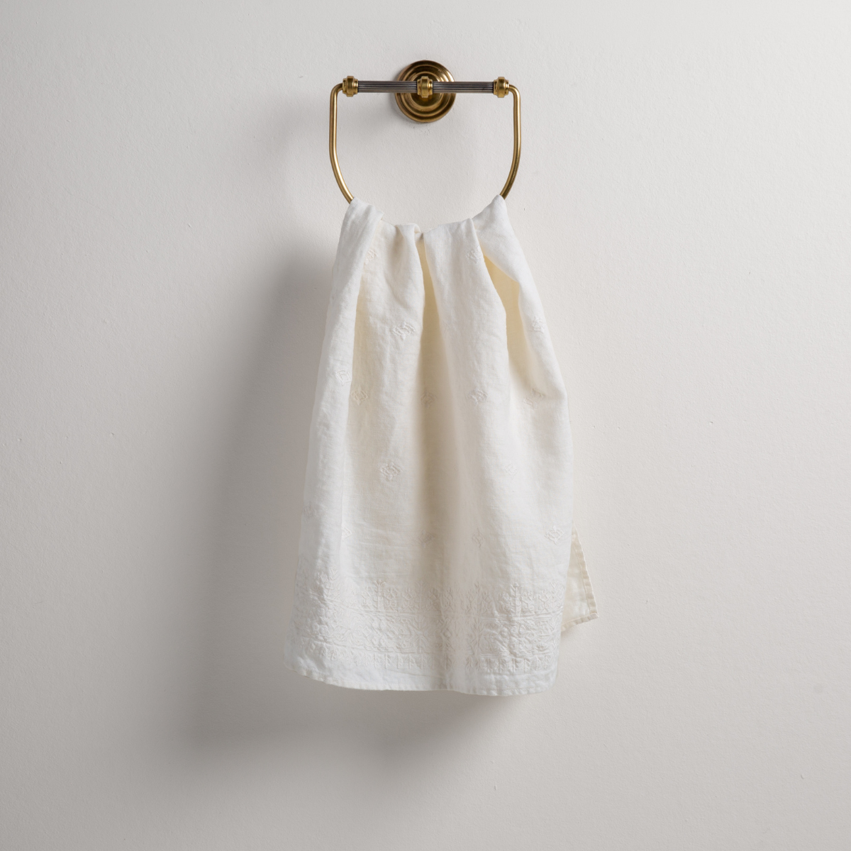Winter White: guest towel draped through a decorative brass towel ring against a white background.