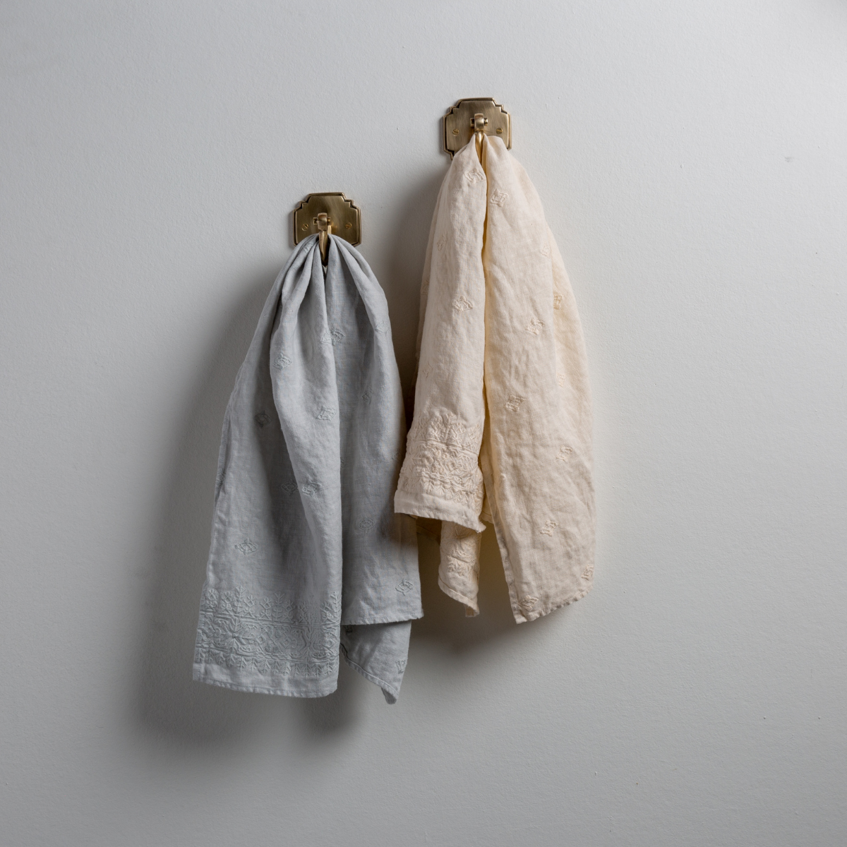 [allvariants]: Two Ines guest towels, draped over decorative hooks against a white wall - cloud and parchment.