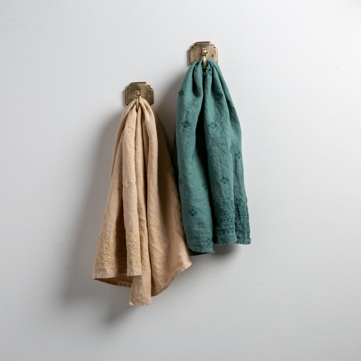 : Two Ines guest towels, draped over decorative hooks against a white wall - honeycomb and jade.