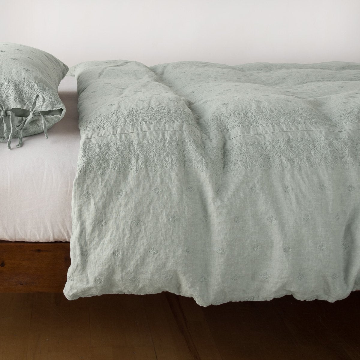 Eucalyptus: lightly rumpled duvet cover on a monochromatic bed against a white background - side view.