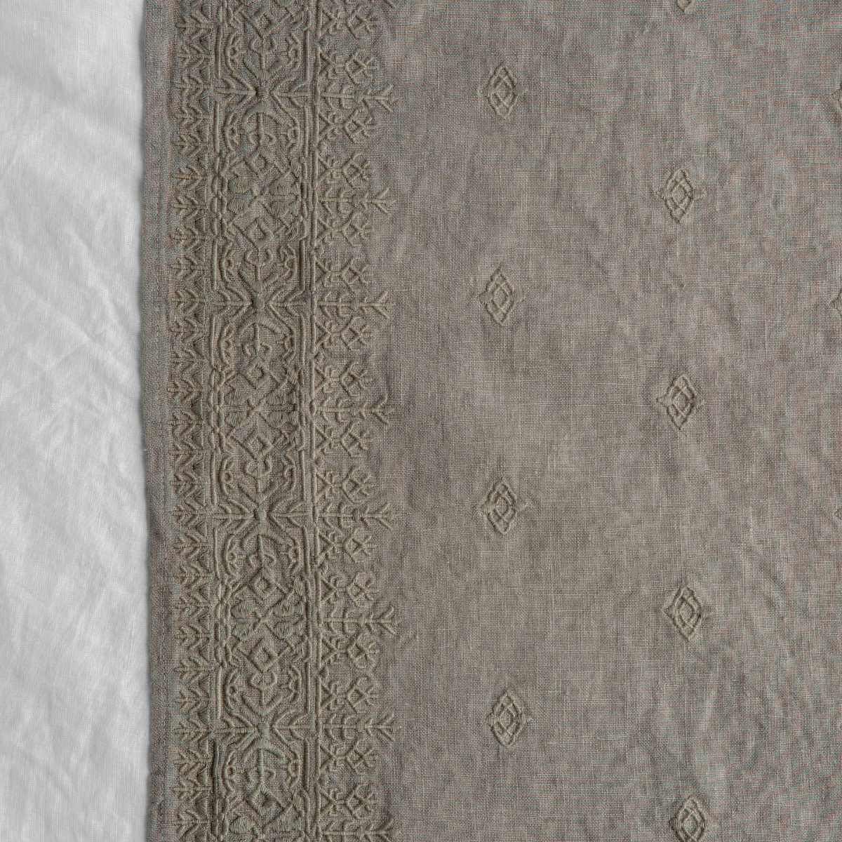 Fog: A close up of Ines, midweight linen with cotton embroidery, in fog, a neutral-warm, soft mid-tone grey. 