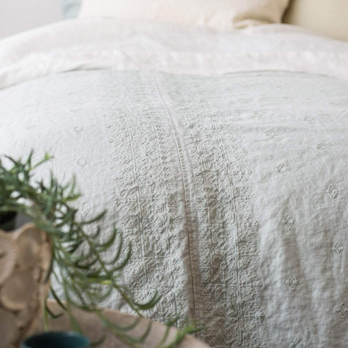 [allvariants]: Eucalyptus duvet cover on a bed with cream-toned sheeting, and greenery visible in the foreground - close-up end of bed view.