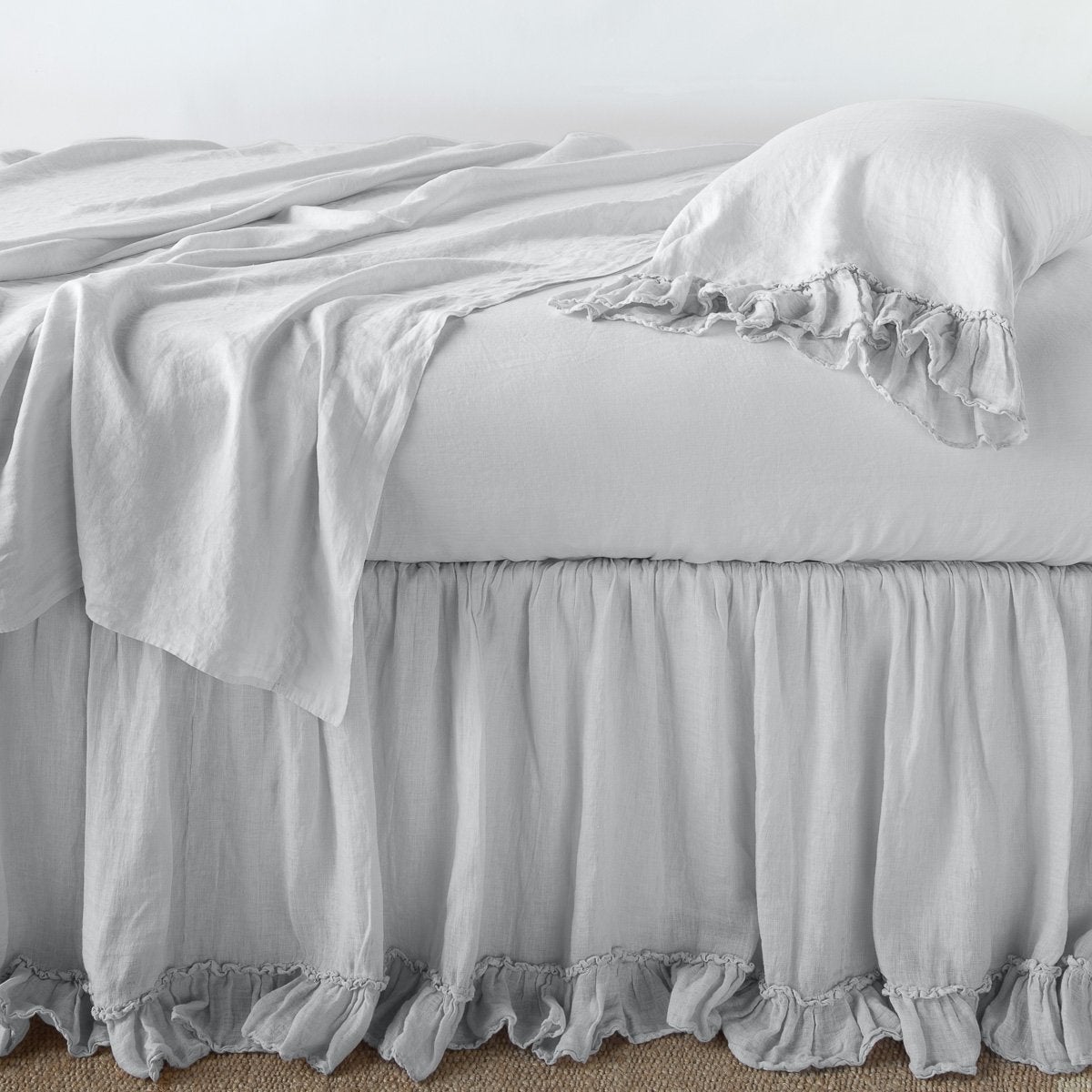 Sterling: bed skirt layered with monochromatic linen sheeting - side view.